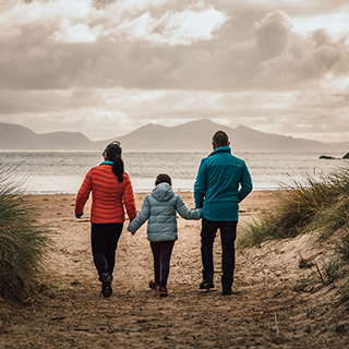 Photo of two adults and a child walking through sand towards the beach (© Natural Resources Wales/Dan Struthers)