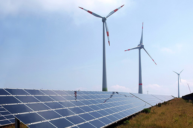 Photograph showing solar panels in the foreground and wind turbines in the background. Image courtesy of Armin Kübelbeck.