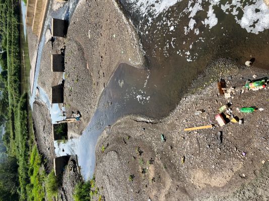 Photograph showing a river with vegetation in the background and visible litter in the foreground (© Isabella Gosetto, JNCC)