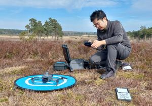 Man kneeling on the ground with a drone on it's launch pad